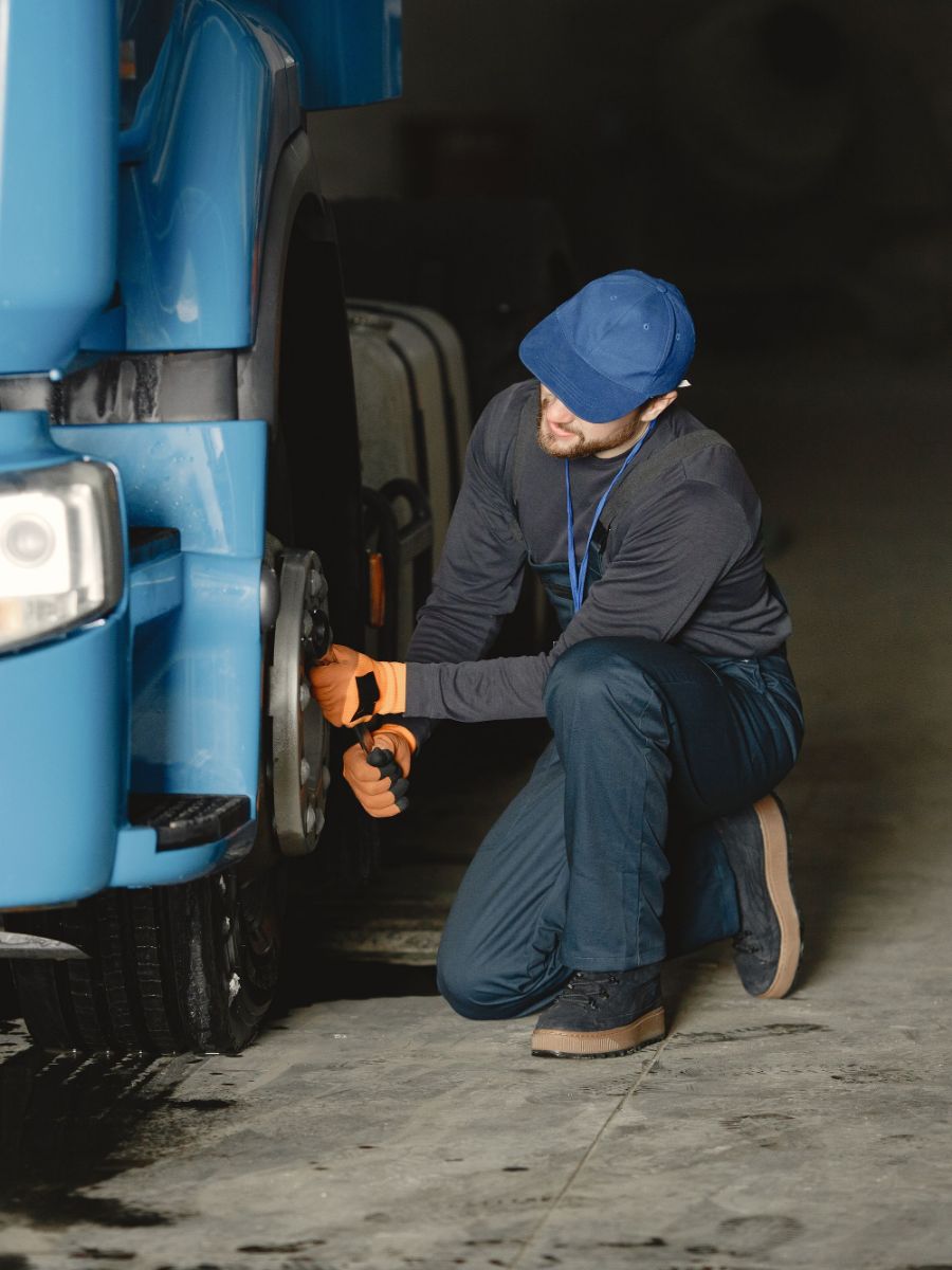 A driver crouching at the front wheel of a truck during a pre-start inspection