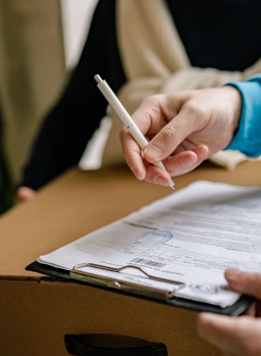 A customer signing a delivery docket on a clipboard resting on a carton