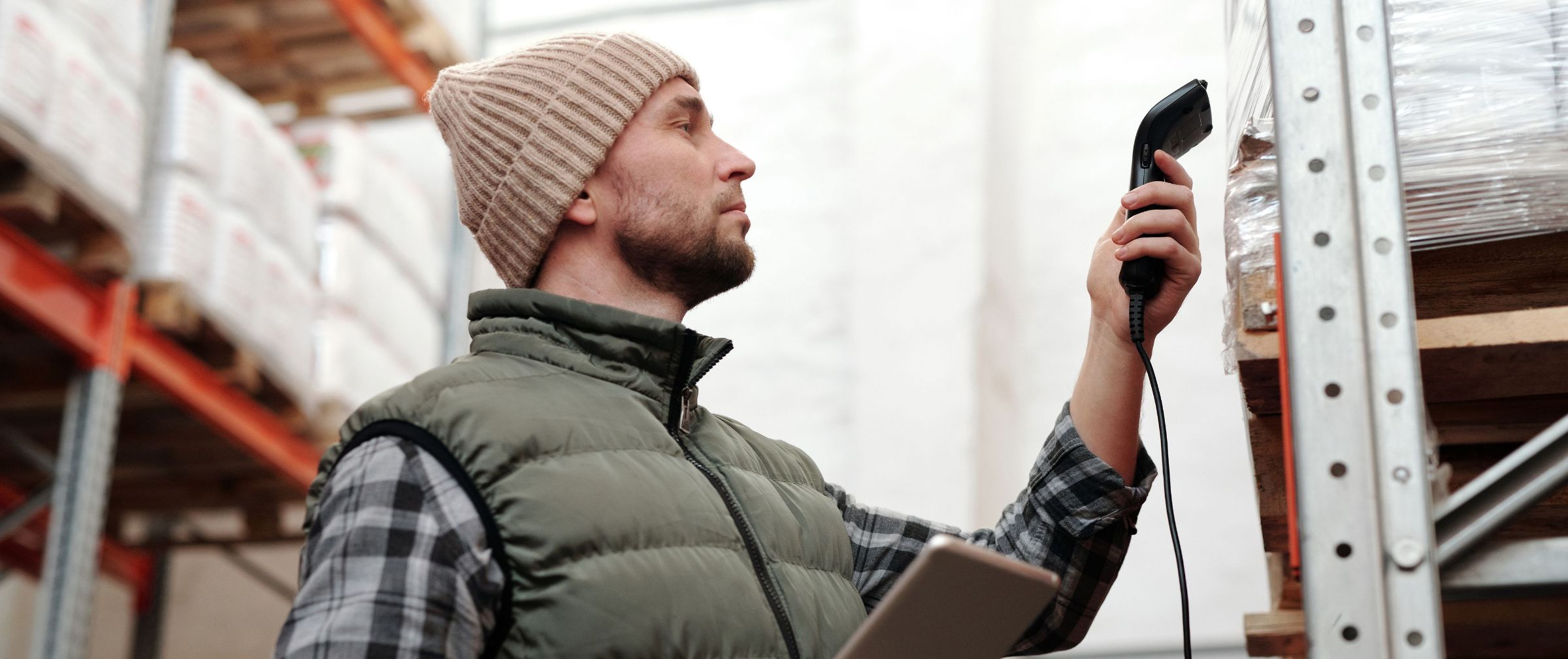 A warehouse worker scanning stock against a handheld scanner and tablet, racking either side